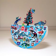 a blue christmas tree with dinosaurs and other holiday decorations on it's side, in front of a white wall