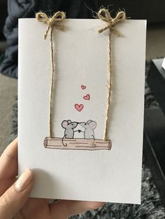 a hand holding a card with two elephants on it and hearts in the sky above them