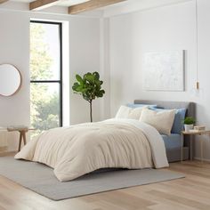 a bedroom with white walls and wood floors, a bed in the middle has a beige comforter on it