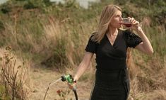 a woman in a black dress drinking from a wine glass while standing next to a bike