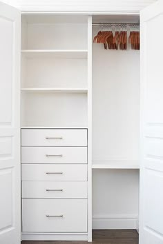 a white closet with drawers and clothes hanging on the wall