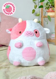 a pink and white stuffed animal sitting on top of a bed next to a green plant