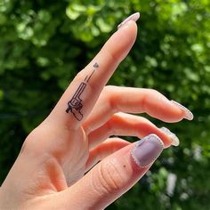 a woman's hand with a small tattoo on her left thumb and fingers, in front of some trees