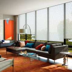 a living room filled with lots of furniture next to tall windows covered in shades of orange and blue