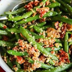 a white bowl filled with green beans covered in toppings on top of a red table