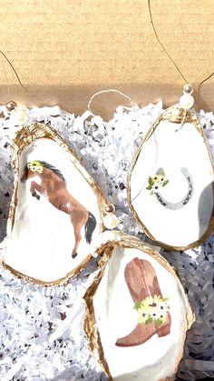 four ornaments with horses painted on them are in a box and one is hanging from a string