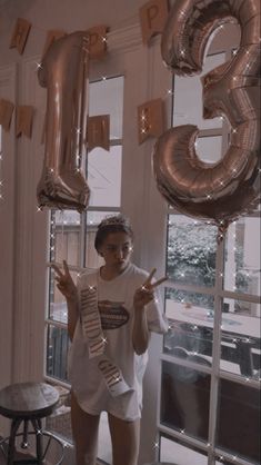 a woman is standing in front of balloons that spell out the number three and pointing at her finger