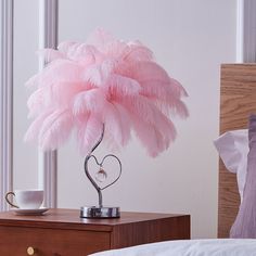 a pink feather lamp on a nightstand next to a bed