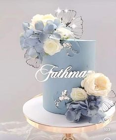 a blue cake with white flowers and butterflies on it's side that says, faithma