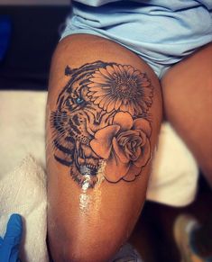 a woman's thigh with a tiger and flowers tattoo on her leg, next to a blue glove