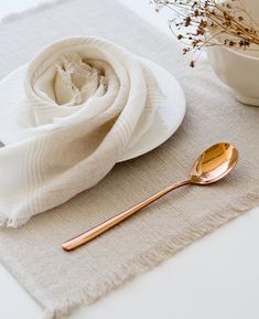 a white cloth with a rose on it next to a gold spoon and bowl filled with dried flowers