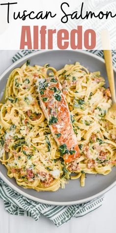 a plate of pasta with salmon and spinach on it, next to a wooden spoon