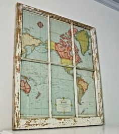 an old window with a world map on the glass in front of it, sitting on a shelf next to a white wall