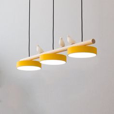 three birds are sitting on top of the yellow light fixture hanging from the ceiling in this room