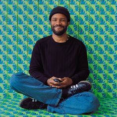 a man sitting on the floor with his feet crossed and holding a cell phone in front of him