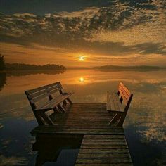 two wooden benches sitting on top of a pier next to the ocean at sunset or dawn