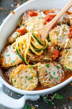 a white casserole dish with zucchini and meatballs in tomato sauce