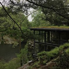 a house with a green roof on top of a cliff next to a lake and forest