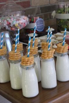 some cookies and milk in small glass jars with blue straws on the top one