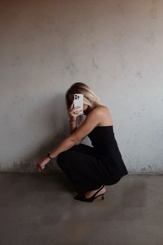 a woman kneeling on the ground taking a selfie with her cell phone in front of her face