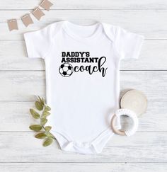 Grab this fun soccer baby bodysuit to announce your pregnancy, give at that next baby shower, or to support your coach on game day! Made specifically with the coach's kid in mind, these bodysuits will get everyone excited for the soccer season and remind the coach how much they are loved by the whole family. ⚜️Care Instructions: - Turn bodysuit inside out and wash on cold - Tumble dry on low temperature - Do not iron directly on the lettering FOLLOW US Pinterest: @thegamedayfamily Instagram: @th Soccer Gift Basket, Girl Baseball Outfit, Cricut Onesies, Baby Boy Pregnancy, Soccer Gift Ideas, Baby Craft Ideas, Crafts For Baby, Funny Baby Shirts, Crossfit Shirts