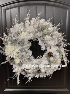 a wreath with white flowers and pine cones on the front door, decorated for christmas