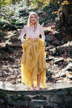 a woman in a yellow skirt standing on a stone wall with her hands on her hips