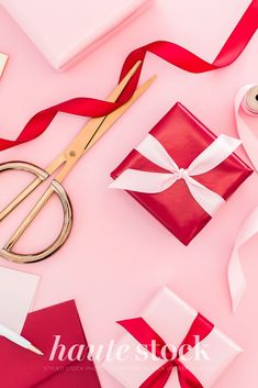 red and white gift wrapping supplies on pink background with ribbon, scissors, and tape