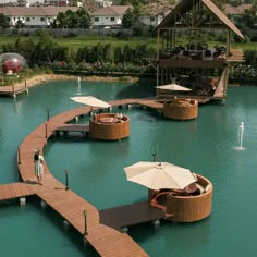 people are standing on wooden walkways in the middle of a body of water with umbrellas over them