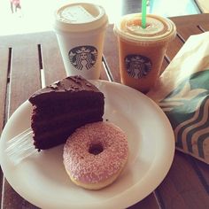 two donuts and a piece of chocolate cake on a plate next to starbucks coffee