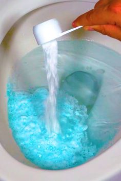 a person is pouring water into a toilet bowl filled with blue liquid and soapy bubbles