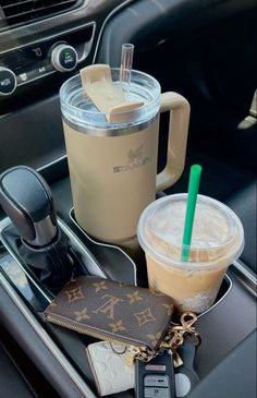 there are two drinks and a cell phone in the cup holder on the car dashboard