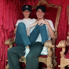 a man and woman sitting on top of a chair in front of a red curtain