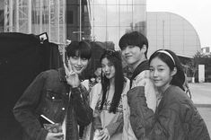 black and white photograph of four young people posing for the camera with one holding a cell phone