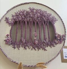 an embroidered wall hanging with purple flowers and trees in the middle, on a white background