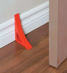 an orange plastic object sitting on the floor next to a wooden door frame and wall