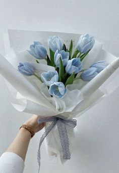 a bouquet of blue tulips is wrapped in white paper and held by a woman's hand