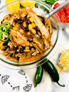 a glass bowl filled with food next to green peppers and lemon wedges on top of a table