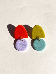 three pairs of colorful earrings sitting on top of a white surface with shadows coming from them