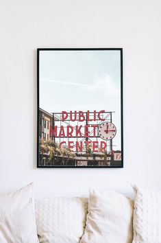 a poster hanging on the wall above a couch in a room with white walls and pillows