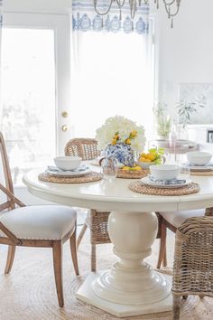 a white table with wicker chairs and plates on it in front of a window