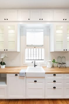 a kitchen with white cabinets and wooden counter tops, along with a window above the sink