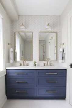 two mirrors on the wall above blue drawers in a white bathroom with gold handles and brass pulls