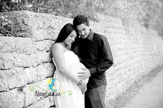 a pregnant couple leaning against a stone wall