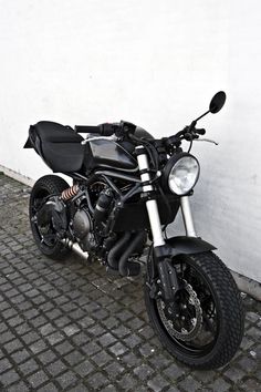 a motorcycle parked next to a white wall on a brick sidewalk in front of a building