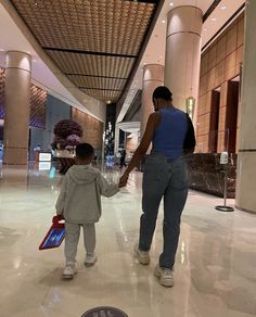 a woman holding the hand of a small child in an airport lobby with flowers on display