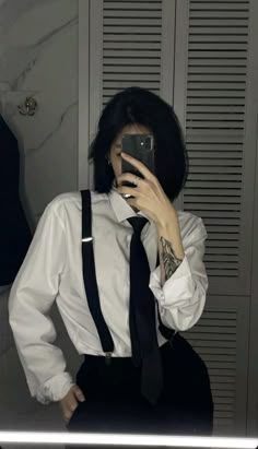 a woman taking a selfie in front of a mirror wearing a tie and suspenders