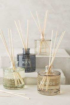 three bottles with reeds in them sitting on a white table next to each other