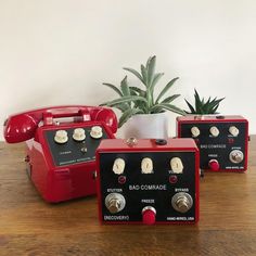 three red telephones sitting next to each other on a wooden table in front of a potted plant