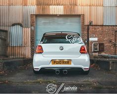 the rear end of a white volkswagen car parked in front of a building with an open garage door